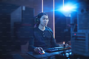 Portrait d’un jeune homme asiatique utilisant un ordinateur dans un cyber-intérieur sombre avec lens flare, espace de copie