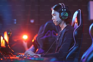 Side view portrait of young Asian pro-gamer playing video games in dark room, copy space