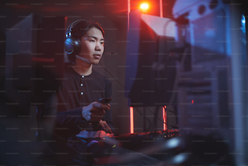Ritratto di giovane uomo asiatico che gioca ai videogiochi usando il turno di corsa in interni cibernetici bui, spazio di copia