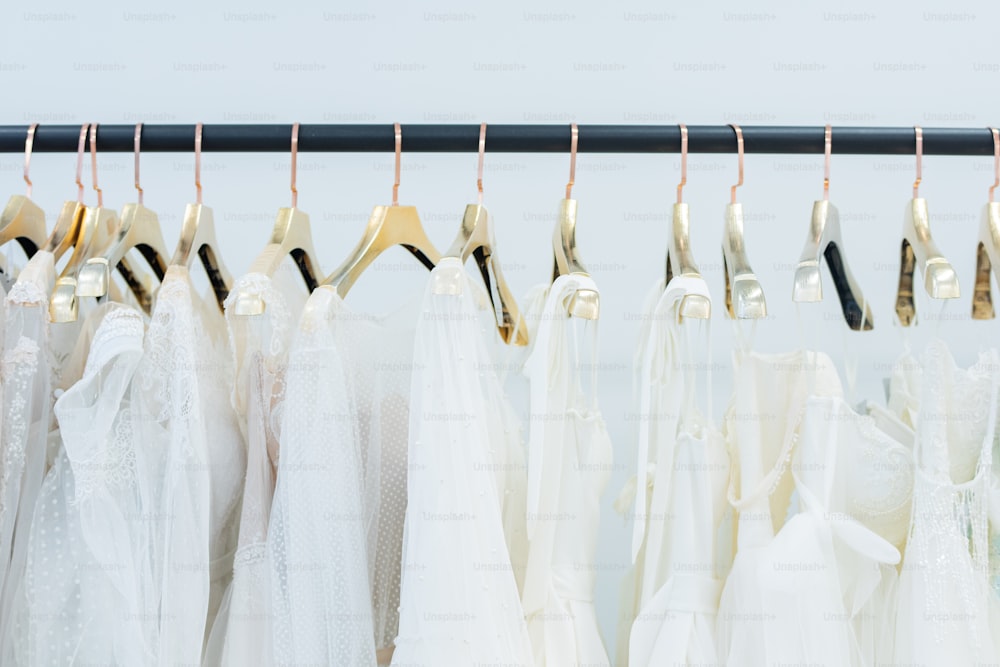 웨딩드레스 가게의 선반에 줄지어 걸려 있는 옷걸이에 다양한 흰색 드레스
