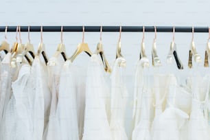 Various white dresses on hangers hanging in row on rack in wedding gown store