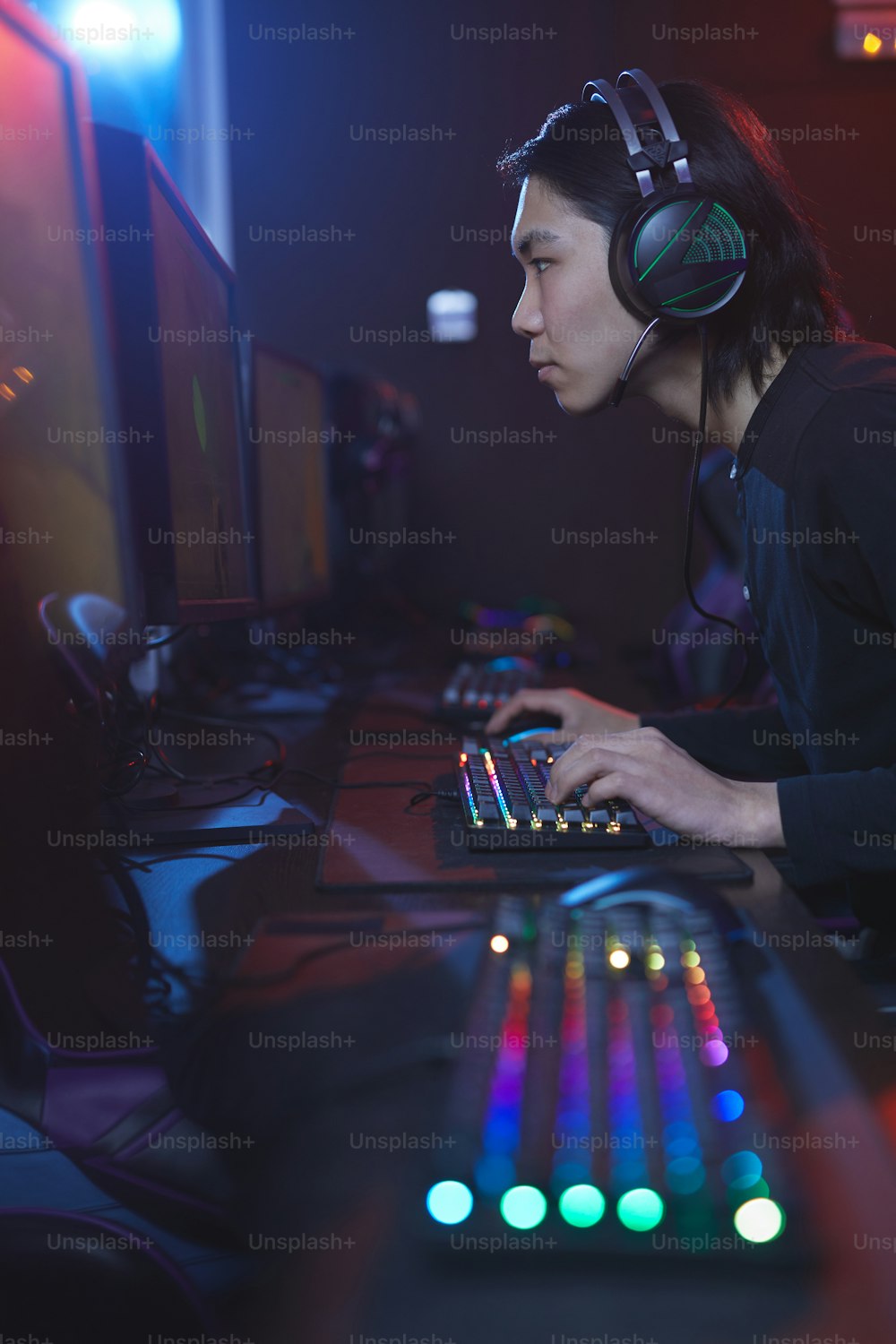 Vertical side view portrait of young Asian man using computer in cyber hacking studio, copy space