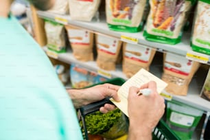 Midsection of male customer checks shopping list in supermarket