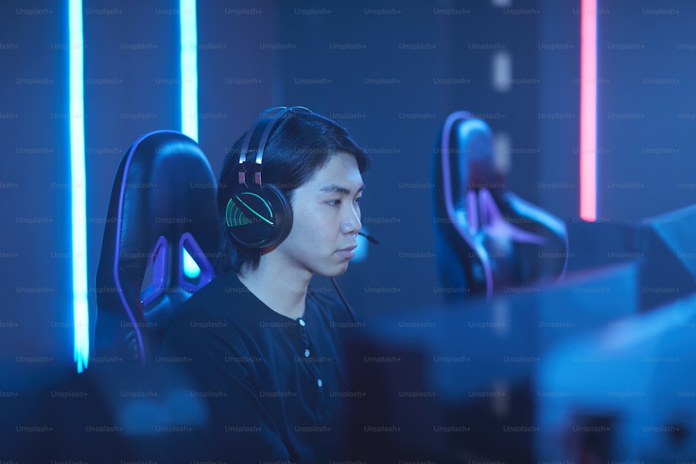 Ritratto della vista laterale del giovane asiatico che parla all'auricolare mentre gioca ai videogiochi nella stanza buia, spazio di copia