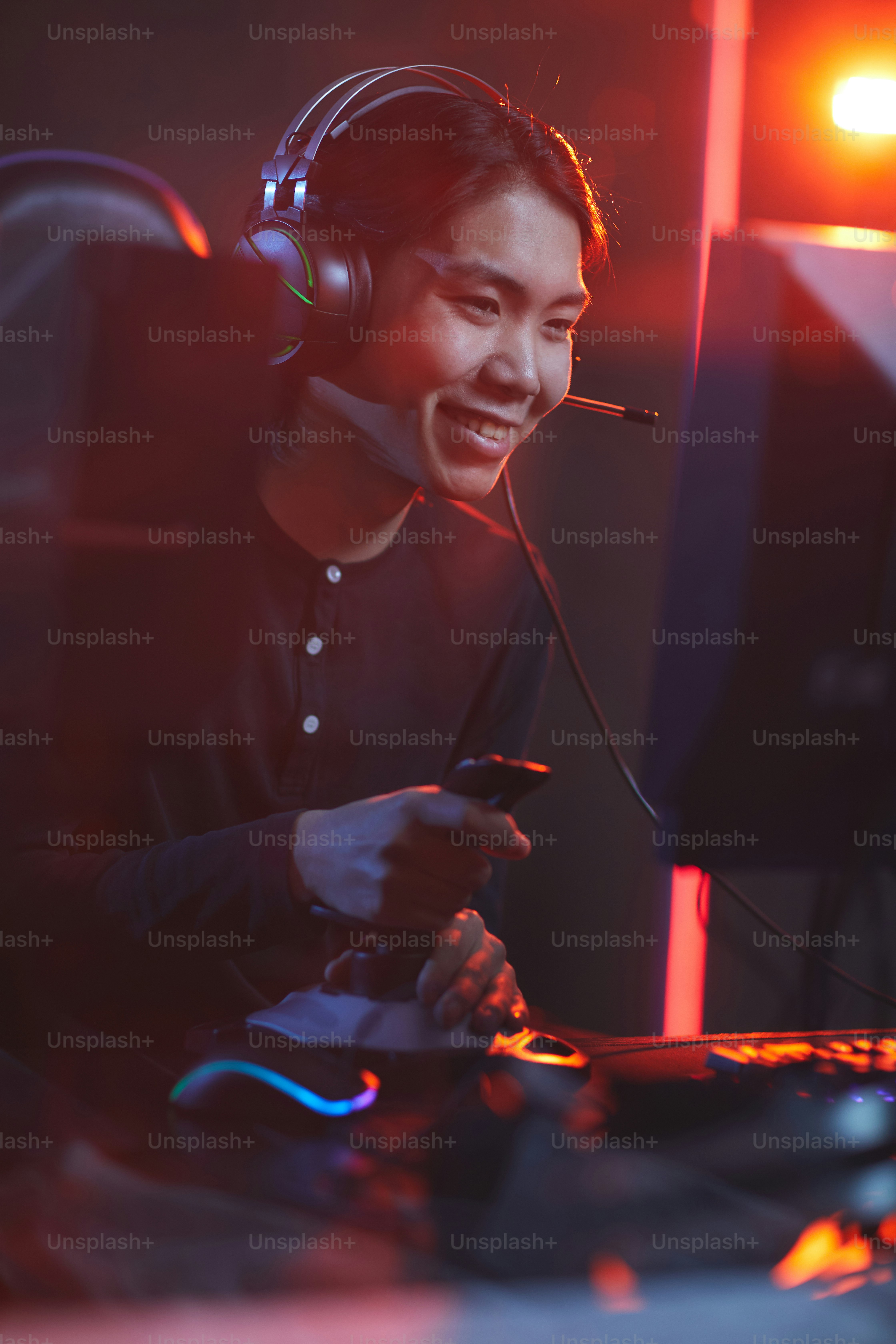 Vertical portrait of smiling Asian man playing video games using racing shift in dark cyber interior