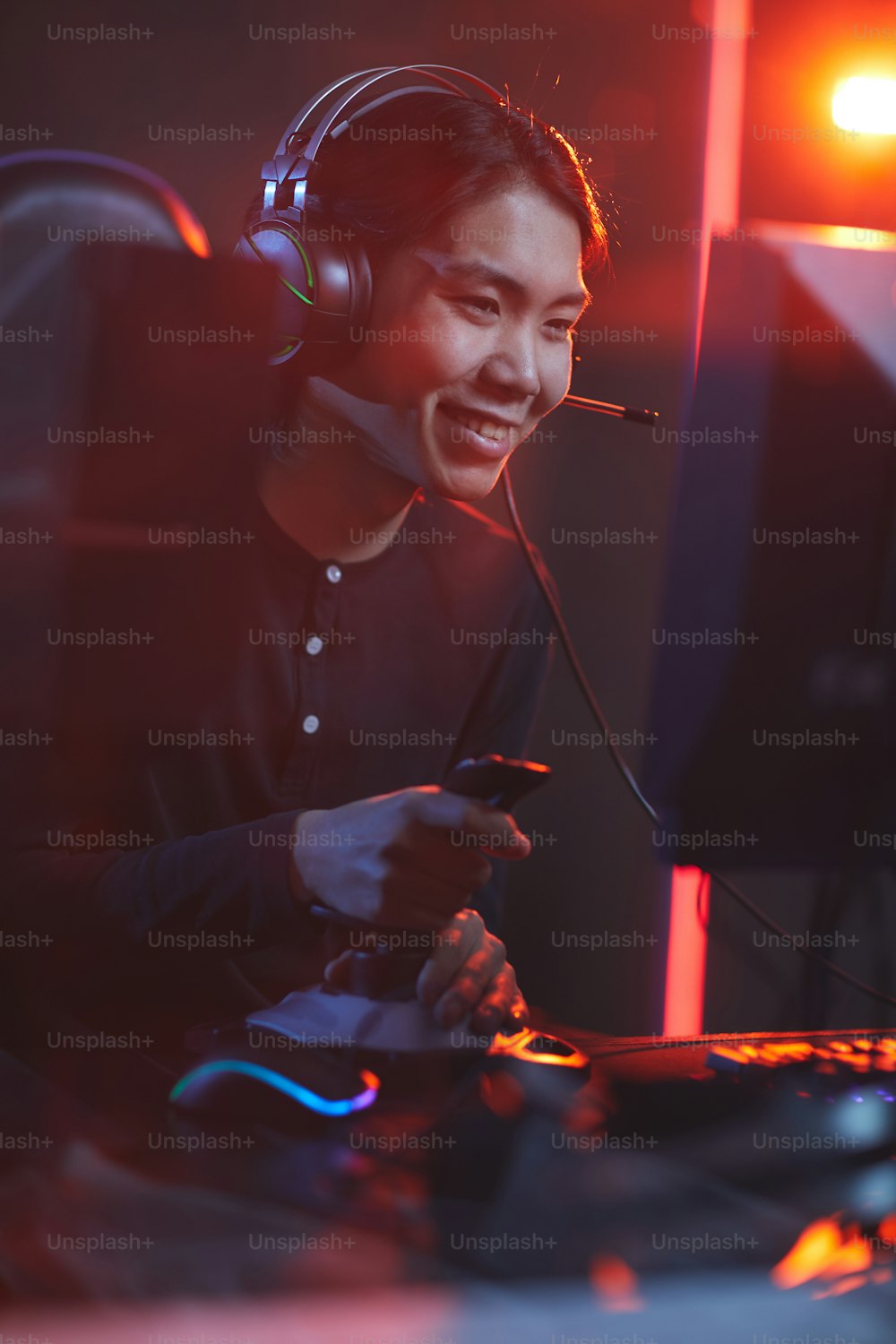 Vertikales Porträt eines lächelnden asiatischen Mannes, der Videospiele mit Rennschicht im dunklen Cyber-Innenraum spielt