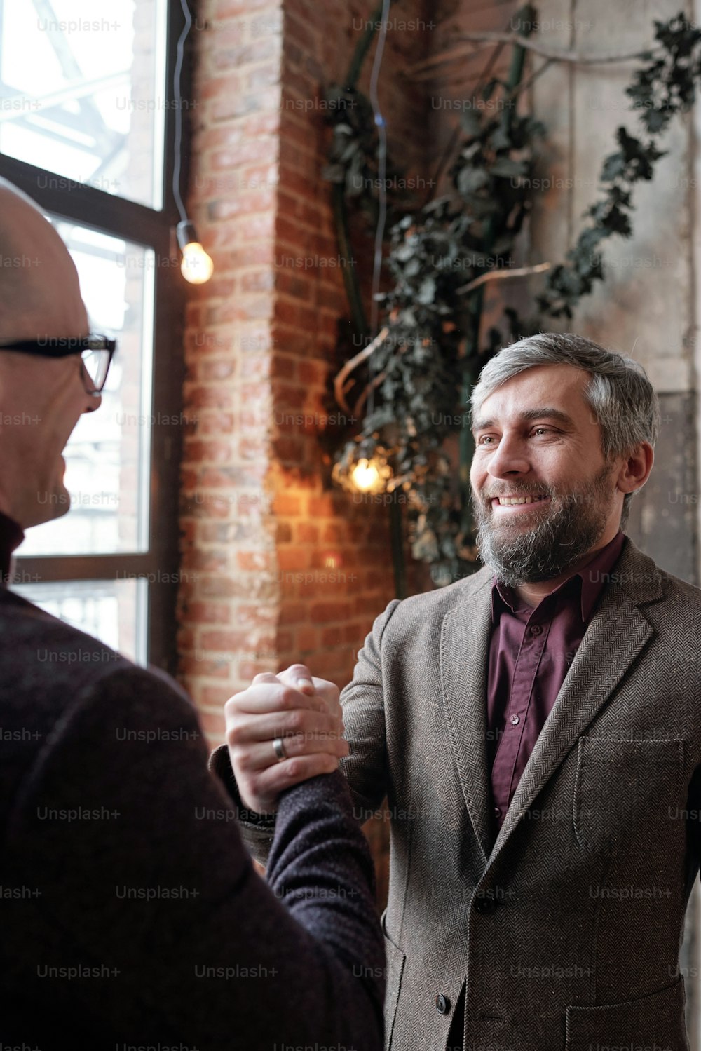 強い関係の象徴として同僚と握手するジャケットを着た笑顔のひげを生やしたビジネスマン
