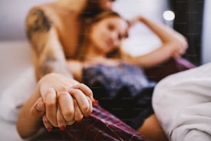 Young passionate handsome couple in love lying in bed in bedroom, holding hands and relaxing.