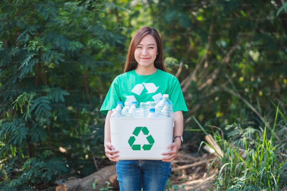 야외에서 쓰레기를 모으고 플라스틱 병이 든 휴지통을 들고 있는 아름다운 아시아 여성