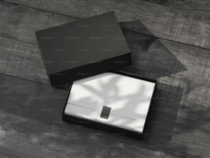 Maquette de boîte cadeau noire ouverte avec du papier d’emballage blanc sur la table en bois à l’extérieur. Rendu 3D