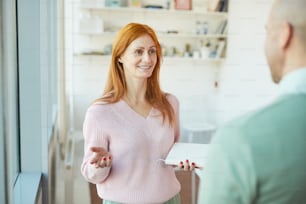 Portrait of smiling businesswoman talking to mature man while standing in modern office, copy space