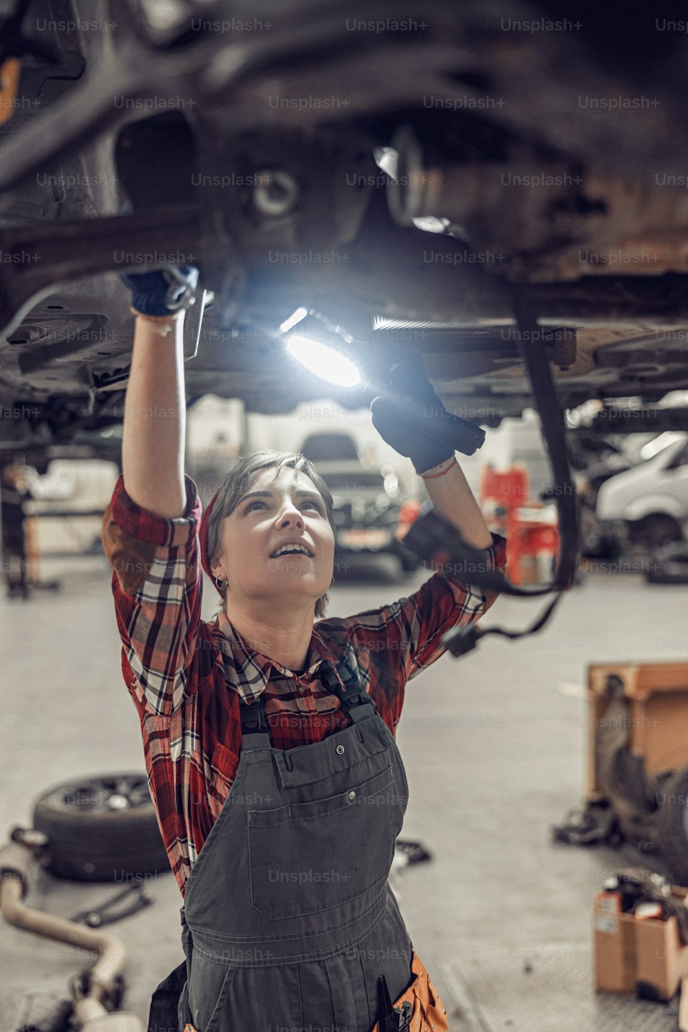 Concentrated female standing under a raised vehicle in a workshop