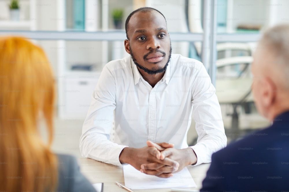 Portrait of contemporary African-American man listening to HR manager during job interview in office, copy space
