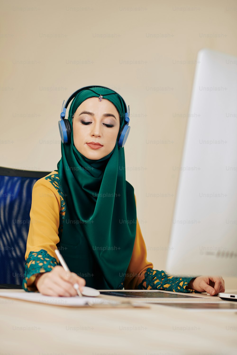 Female entrepreneur in hijab listening to music in headphones when working on project