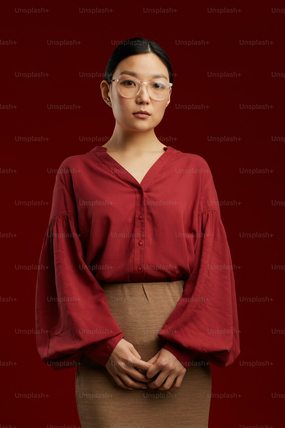 Professional portrait of elegant Asian woman standing by maroon background and looking at camera