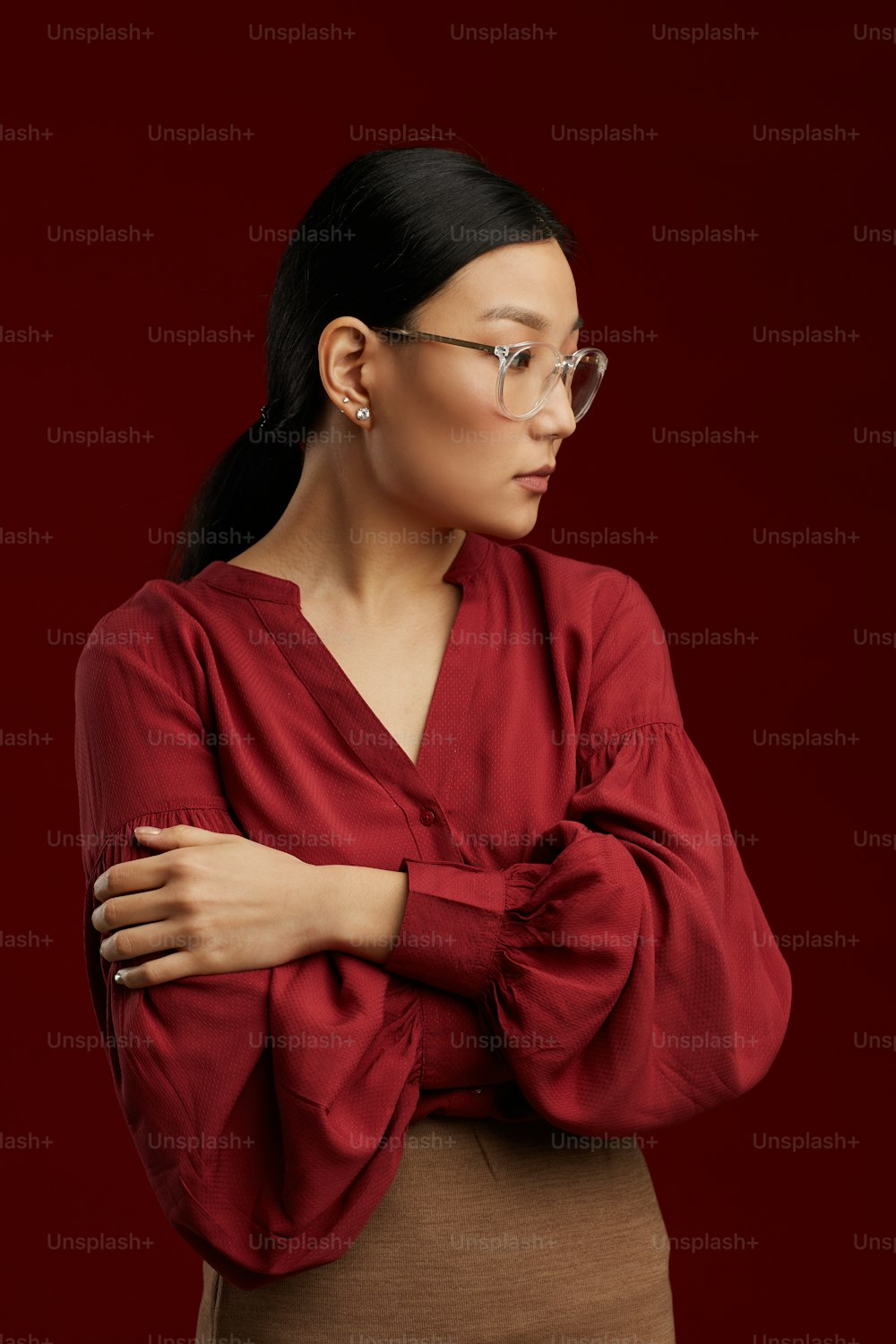 Retrato de cintura para arriba de una mujer asiática con blusa roja posando rígidamente contra el fondo granate en el estudio
