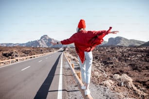 Retrato de estilo de vida de uma jovem vestida elegantemente de vermelho caminhando na cerca da estrada no meio do vale vulcânico em um dia ensolarado. Estilo de vida despreocupado e conceito de viagem