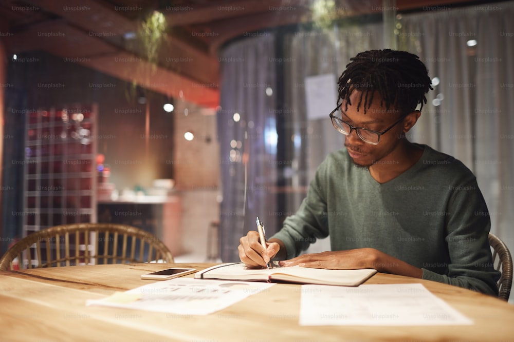 Portrait d’un homme afro-américain contemporain travaillant avec des documents assis à table dans un bureau, espace de copie