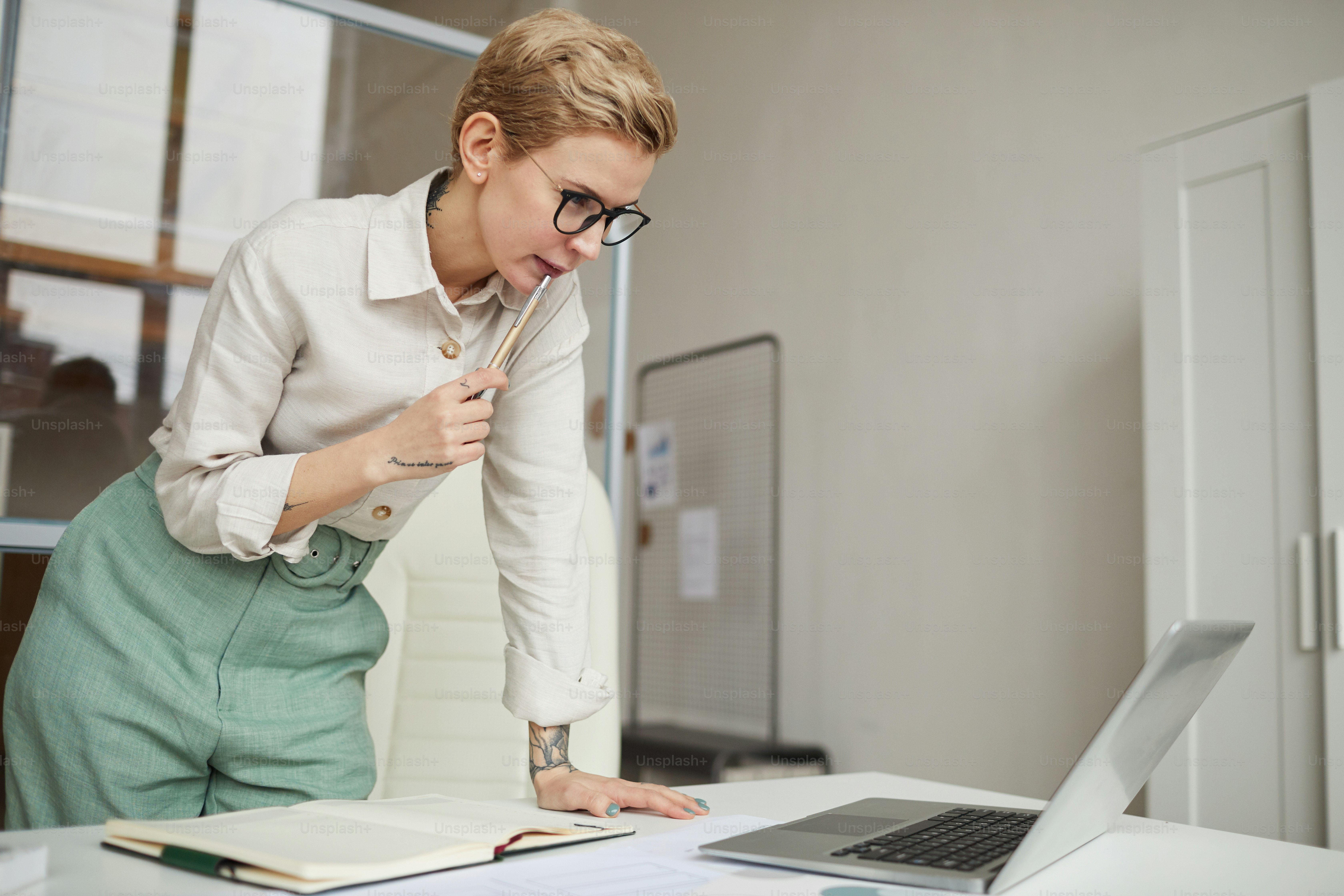 Portrait of modern businesswoman leaing over deskwhile looking at laptop screen in office, copy space