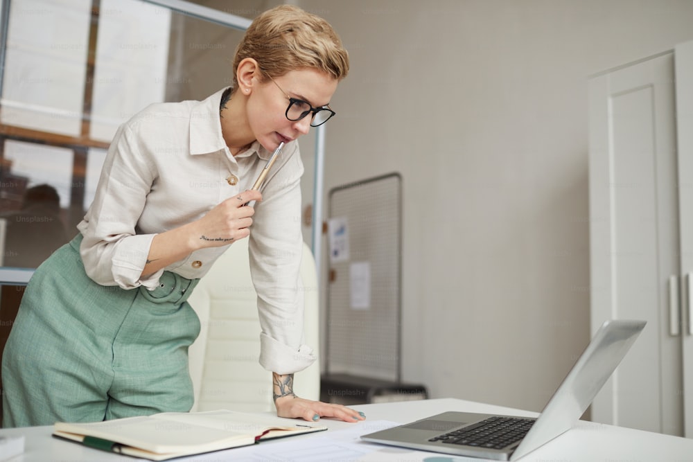 Retrato de una mujer de negocios moderna que se desliza sobre el escritorio mientras mira la pantalla de la computadora portátil en la oficina, copie el espacio