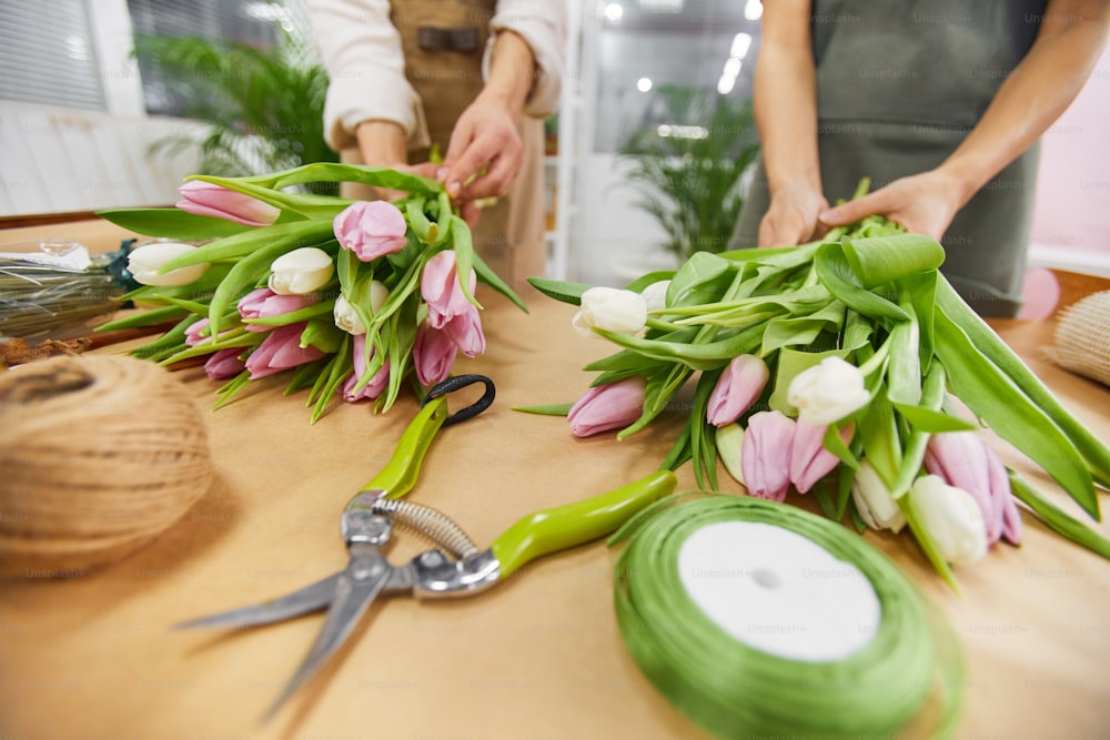 Close up de duas jovens irreconhecíveis organizando buquês de tulipas e composições florais para a temporada de primavera enquanto trabalham em floricultura, espaço de cópia