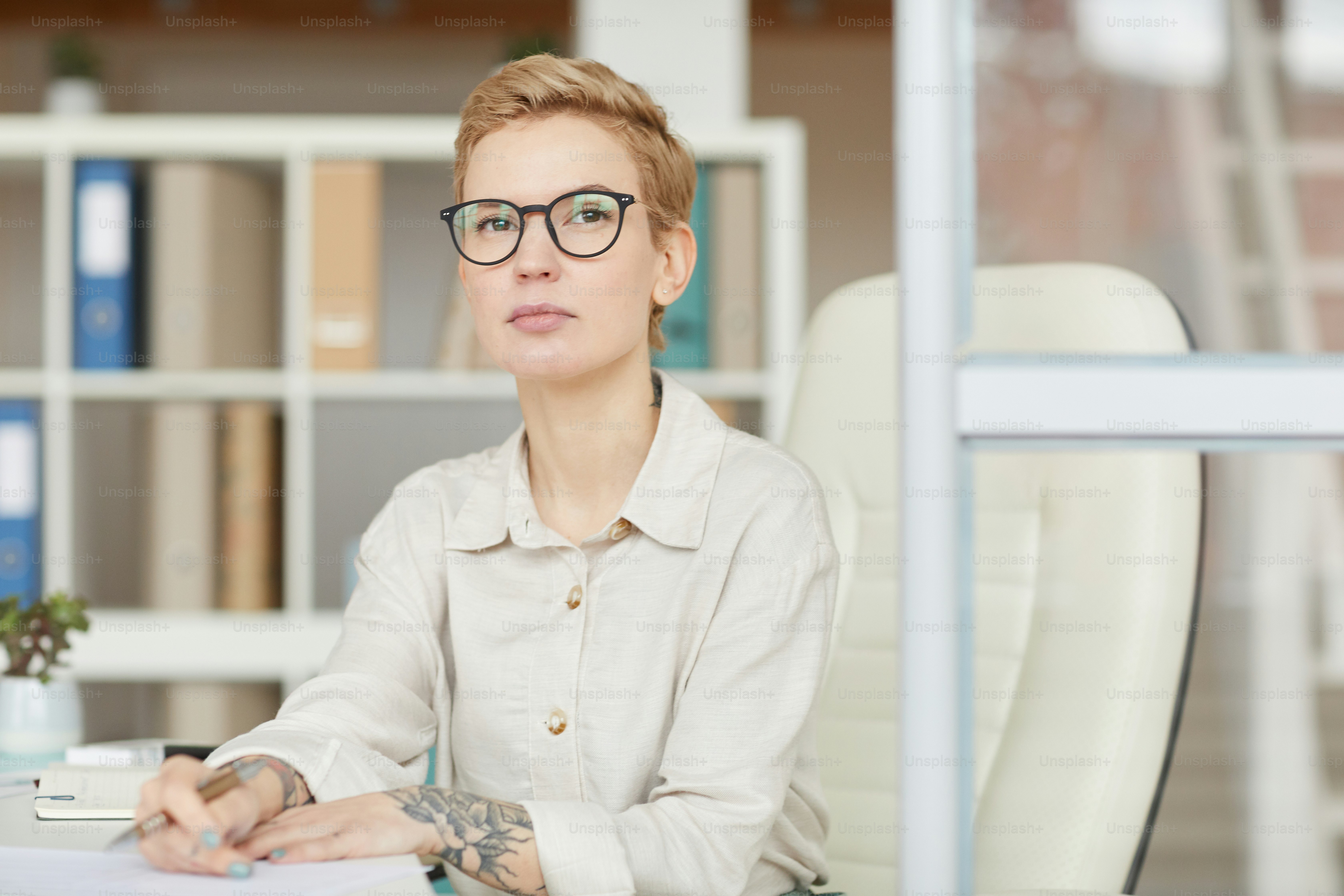 Portrait of confident tattoed businesswoman looking at camera while sitting at desk in office, copy space