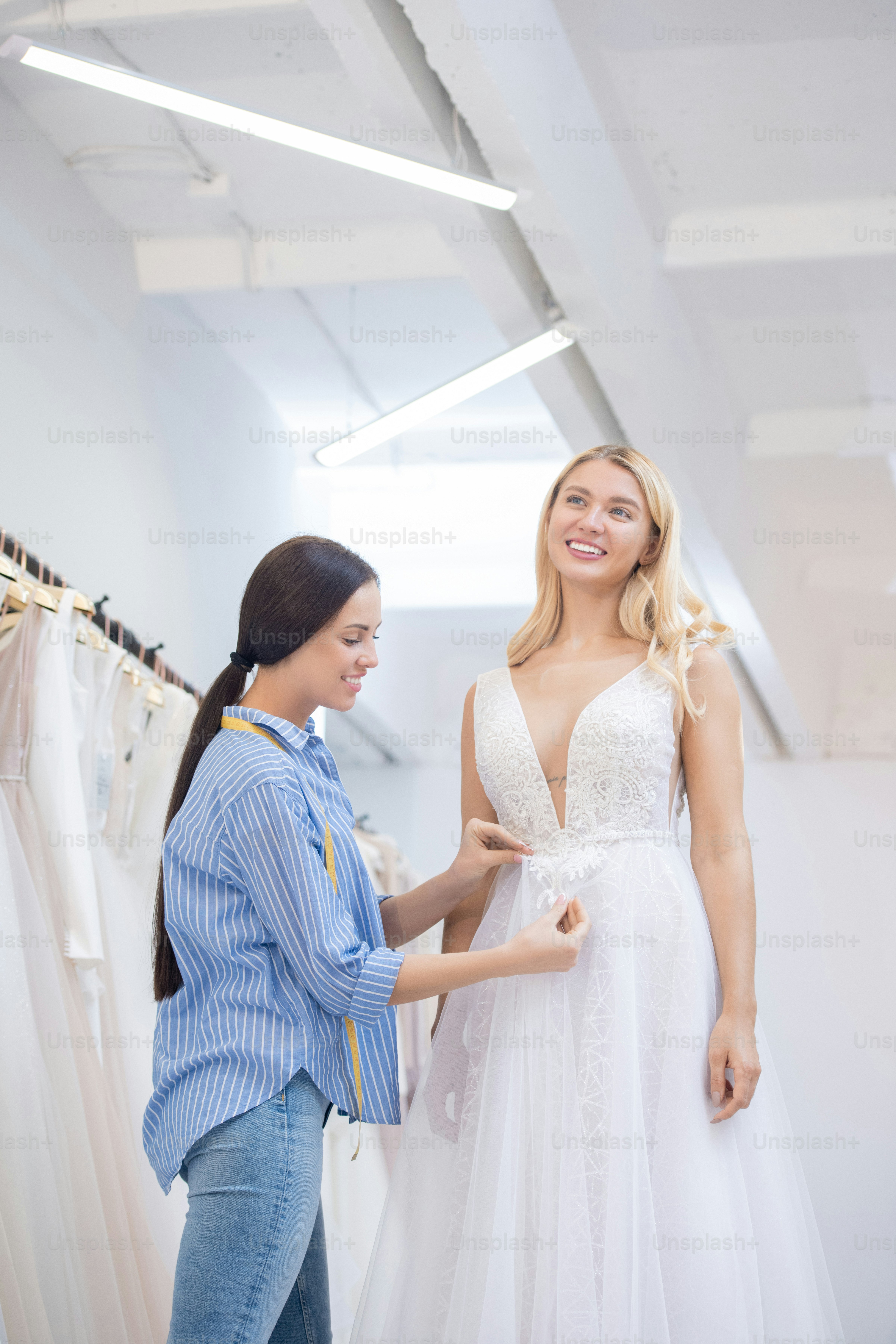 Professional dressmaker fixing beautiful dress decoration element while happy customer standing still
