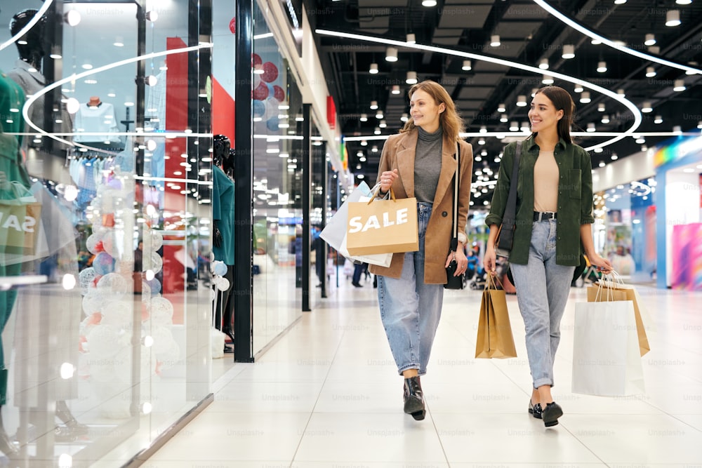 Meninas atraentes felizes em roupas casuais andando sobre o shopping e desfrutando de compras juntos