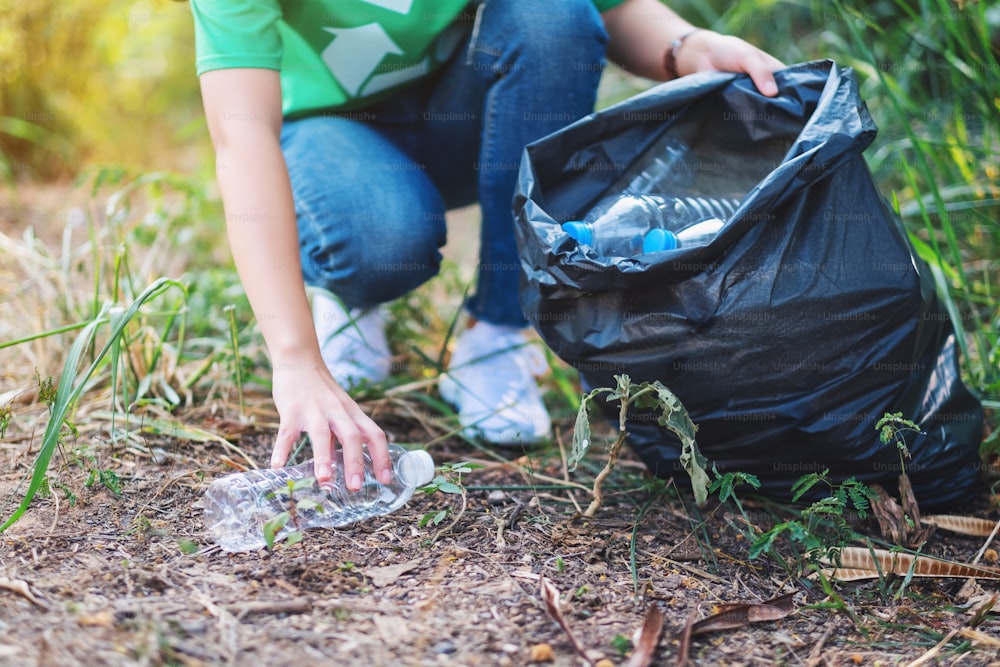 Closeup image of a woman picking up garbage plastic bottles into a bag for recycling concept