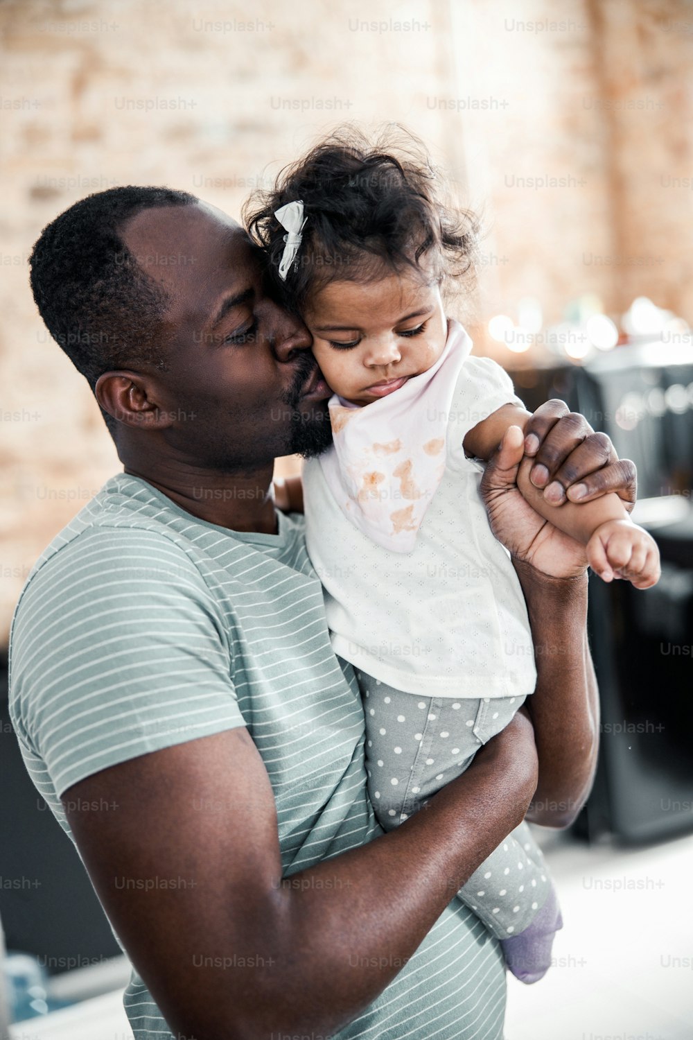 Loving father holding adorable baby girl in arms and placing kiss on her cheek stock photo