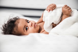 Nahaufnahme eines niedlichen neugeborenen Kindes, das unter einer weißen Decke liegt und sich ein Kamerafoto ansieht