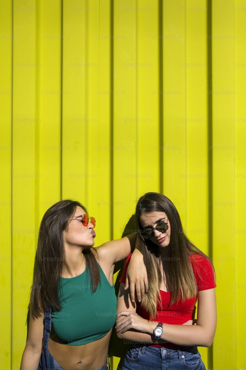 Two cute casual young women fooling around in front of the yellow wall