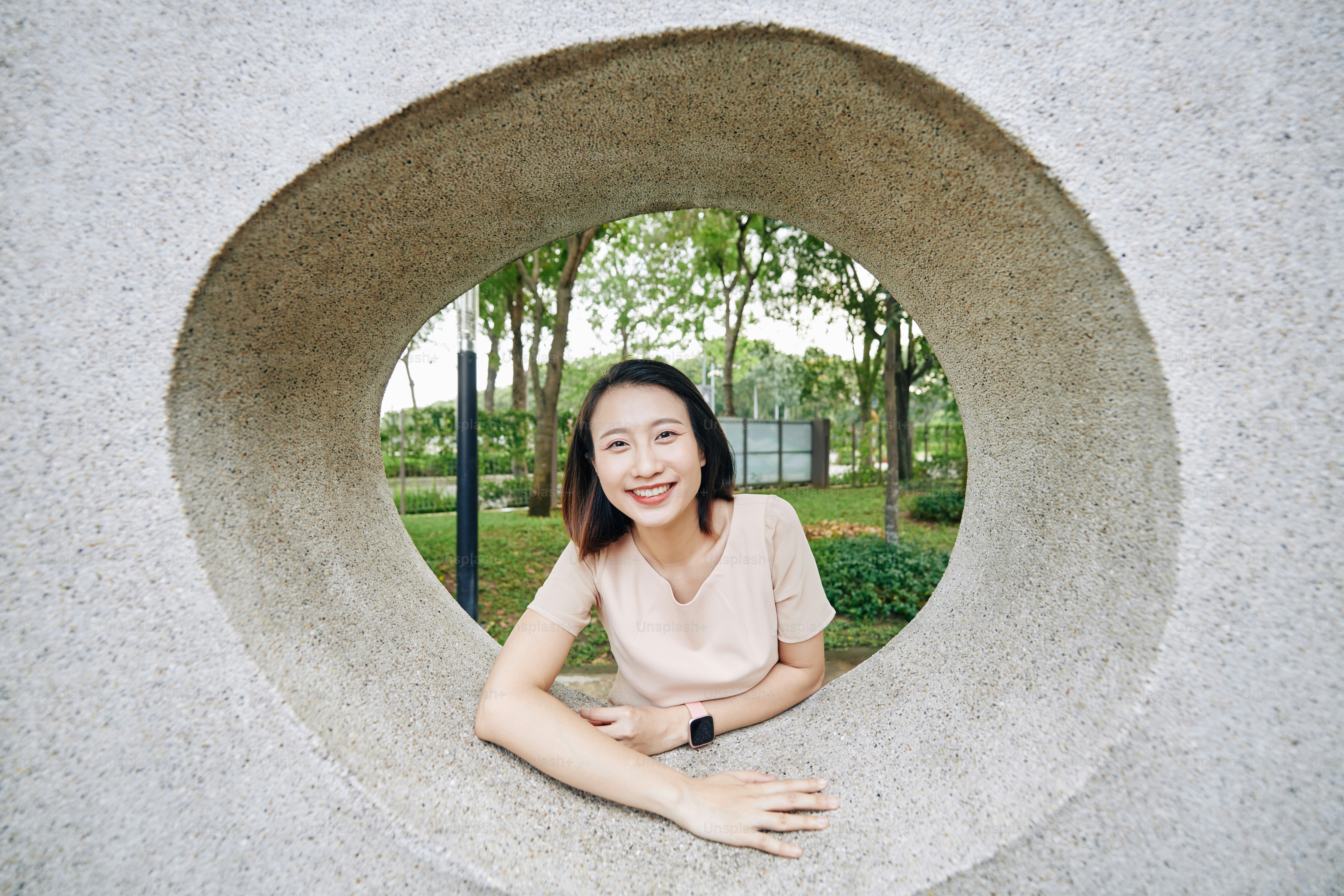 Portrait of smiling pretty young Vietnamese woman looking through hole in concrete wall