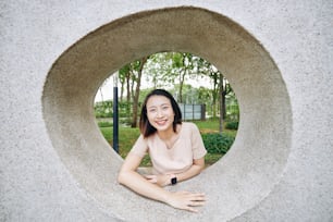 Portrait of smiling pretty young Vietnamese woman looking through hole in concrete wall