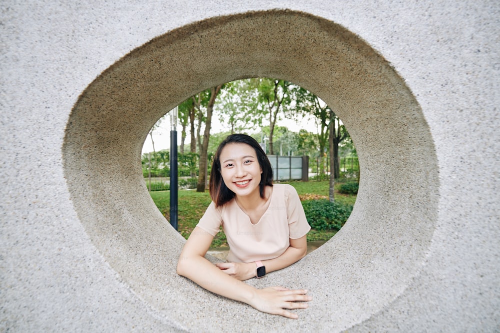 Retrato de una joven vietnamita sonriente mirando a través del agujero en la pared de hormigón