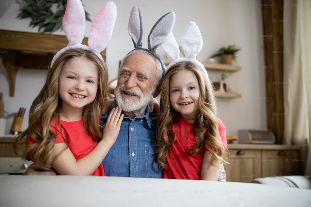 Positive elderly man sitting between his twin granddaughters and looking happy