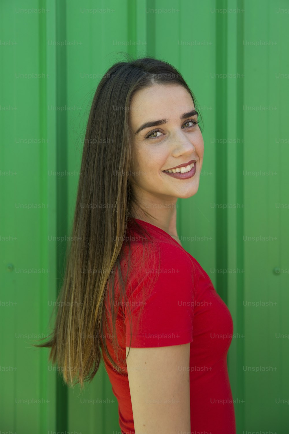 Trendy young woman standing by the green wall on a hot summer day