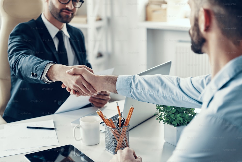 Close up of two young men in formalwear shaking hands while sitting in the office