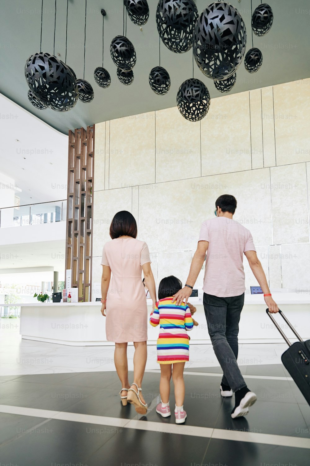 Family of three with big suitcase walking to hotel reception, view from the back