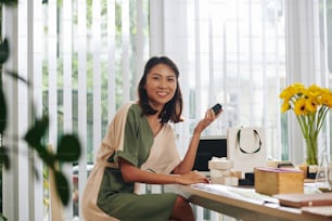 Positive pretty young businesswoman sitting at office desk and packing handmade soaps for customers