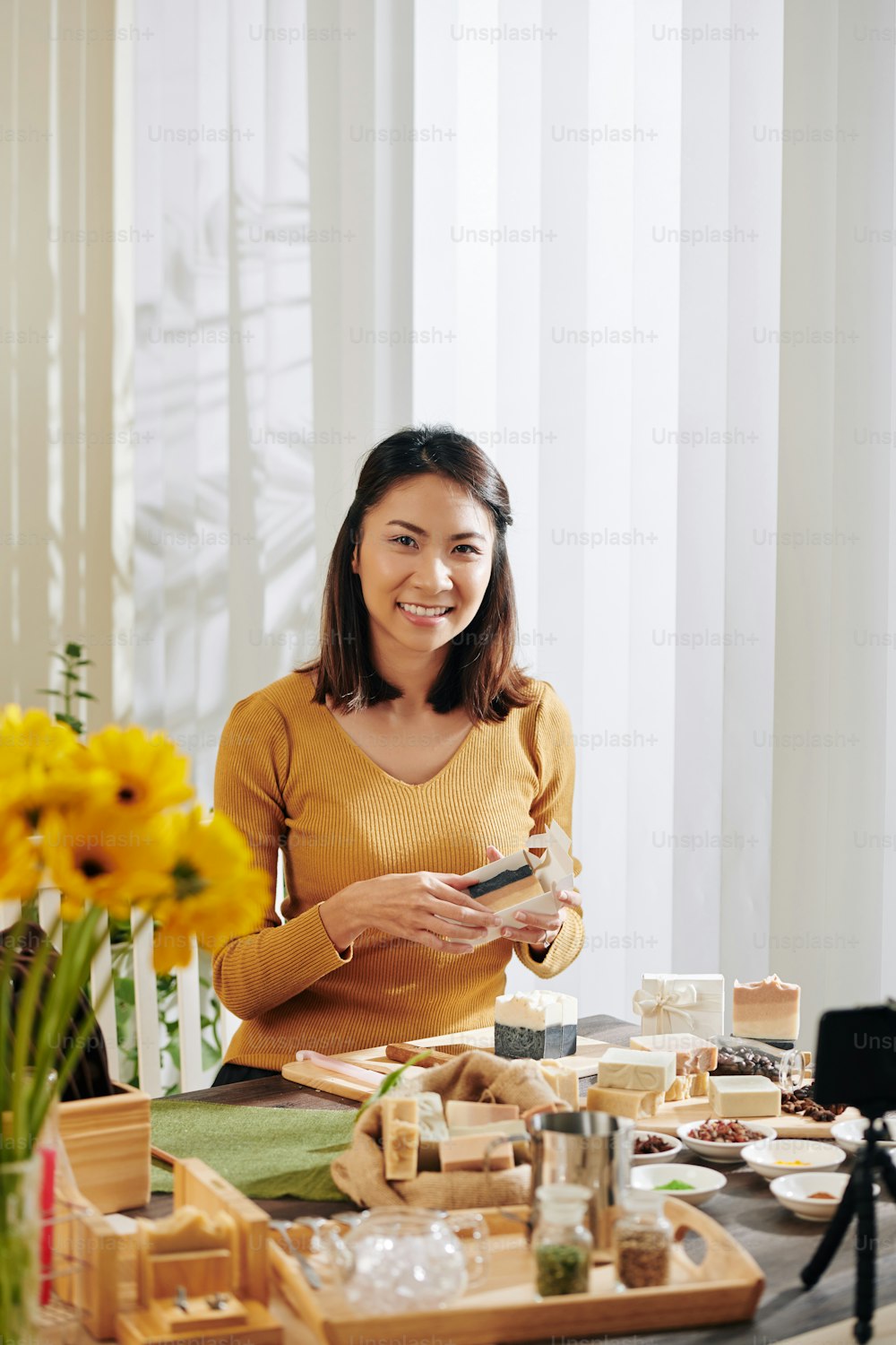 Portrait of cheerful young Asian woman putting soap she made at home in cardboard boxes