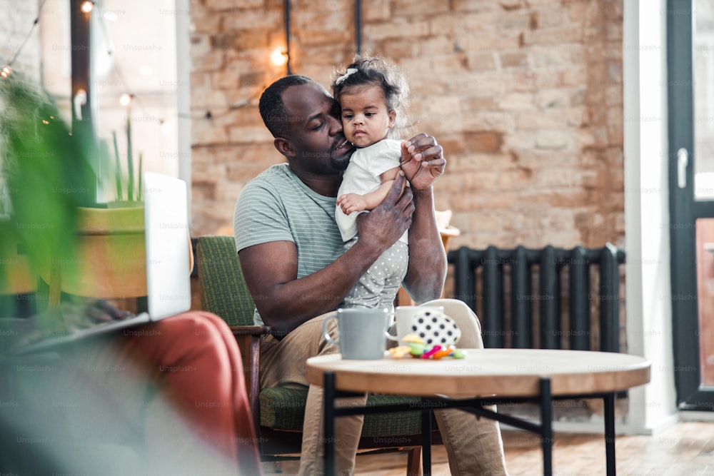 안락의자에 앉아 사랑스러운 여자 아기를 안고 있는 아프리카계 미국인 남자 스톡 사진