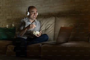 Glücklicher Mann, der sich nachts zu Hause entspannt und einige Fernsehsendungen auf einem Streaming-Dienst sieht, während er Popcorn isst