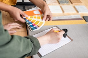 Hands of female designer holding palette over table while showing colors to colleague during work over new order or project at meeting