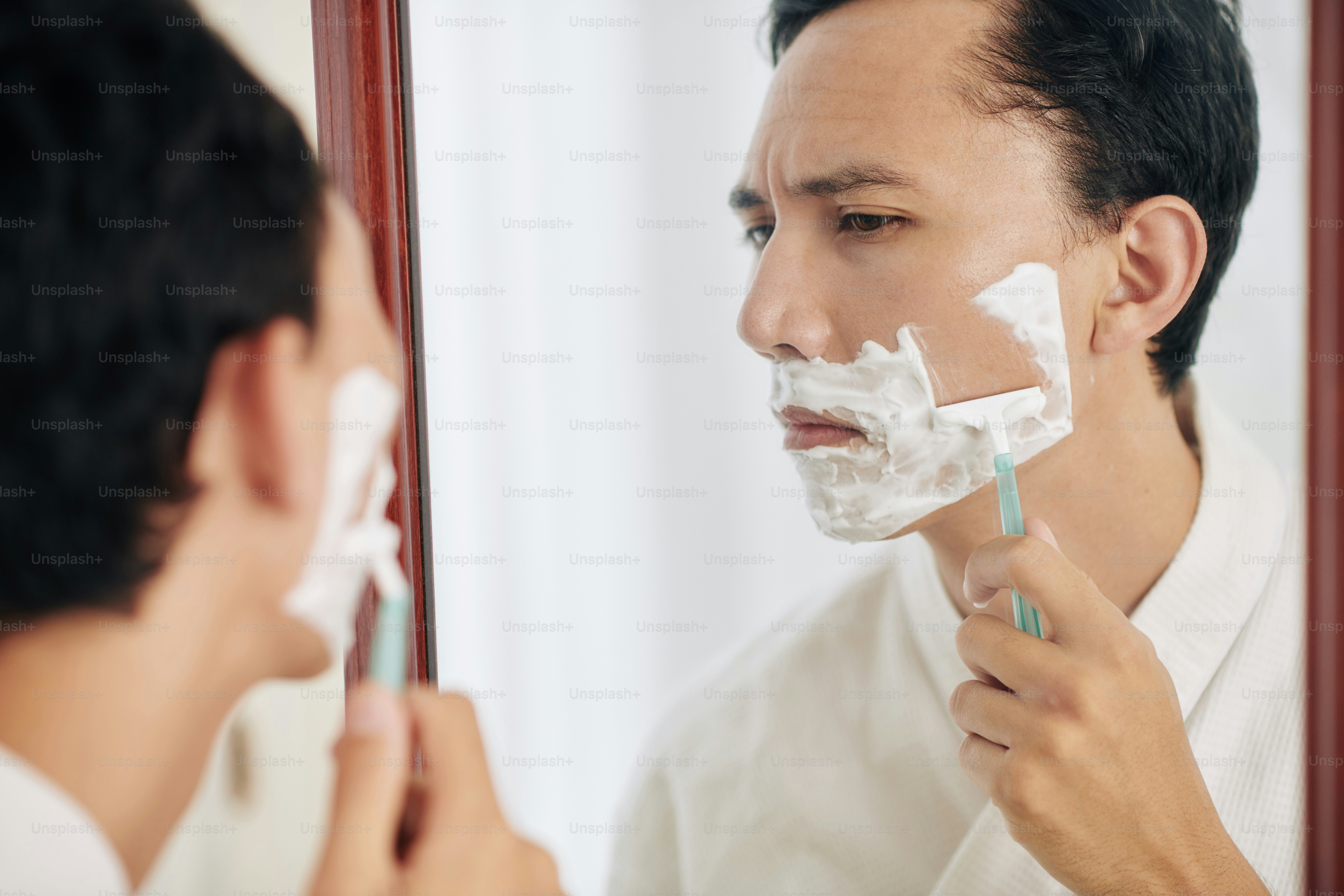 Serious frowning man in waffle town looking at mirror when shaving in ...