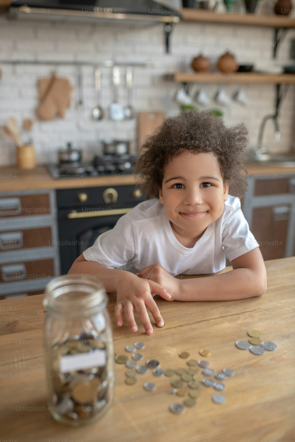 Savings. Cute curly-haired kid in a white tshirt counting his savings