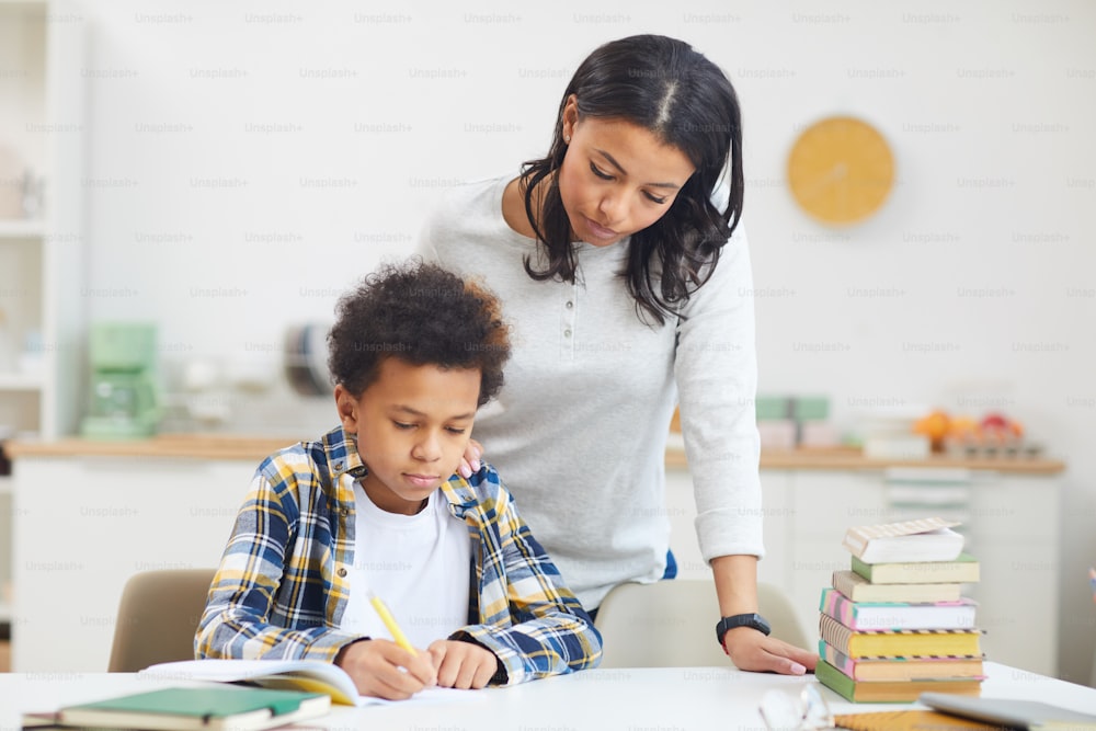 Portrait of young African-American mother helping boy while studying at home, copy space