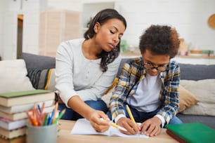 Portrait of modern African woman helping son studying at home, remote education concept