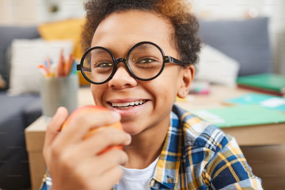 Close up portrait of cute African boy wearing glasses and holding apple while looking at camera