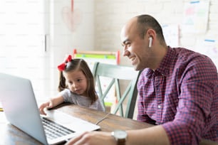 Father and daughter wearing earphones and watching something funny on a laptop computer at home